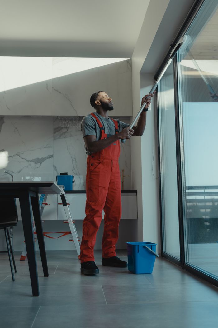A man wearing coveralls is cleaning a large window inside a sleek, contemporary home interior.