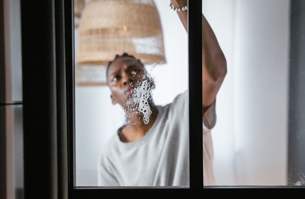Un homme adulte nettoie une fenêtre en verre à l’intérieur, en mettant l’accent sur les tâches ménagères et la propreté.